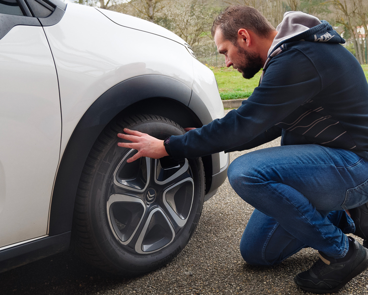 Personne insepctant les pneus de voiture